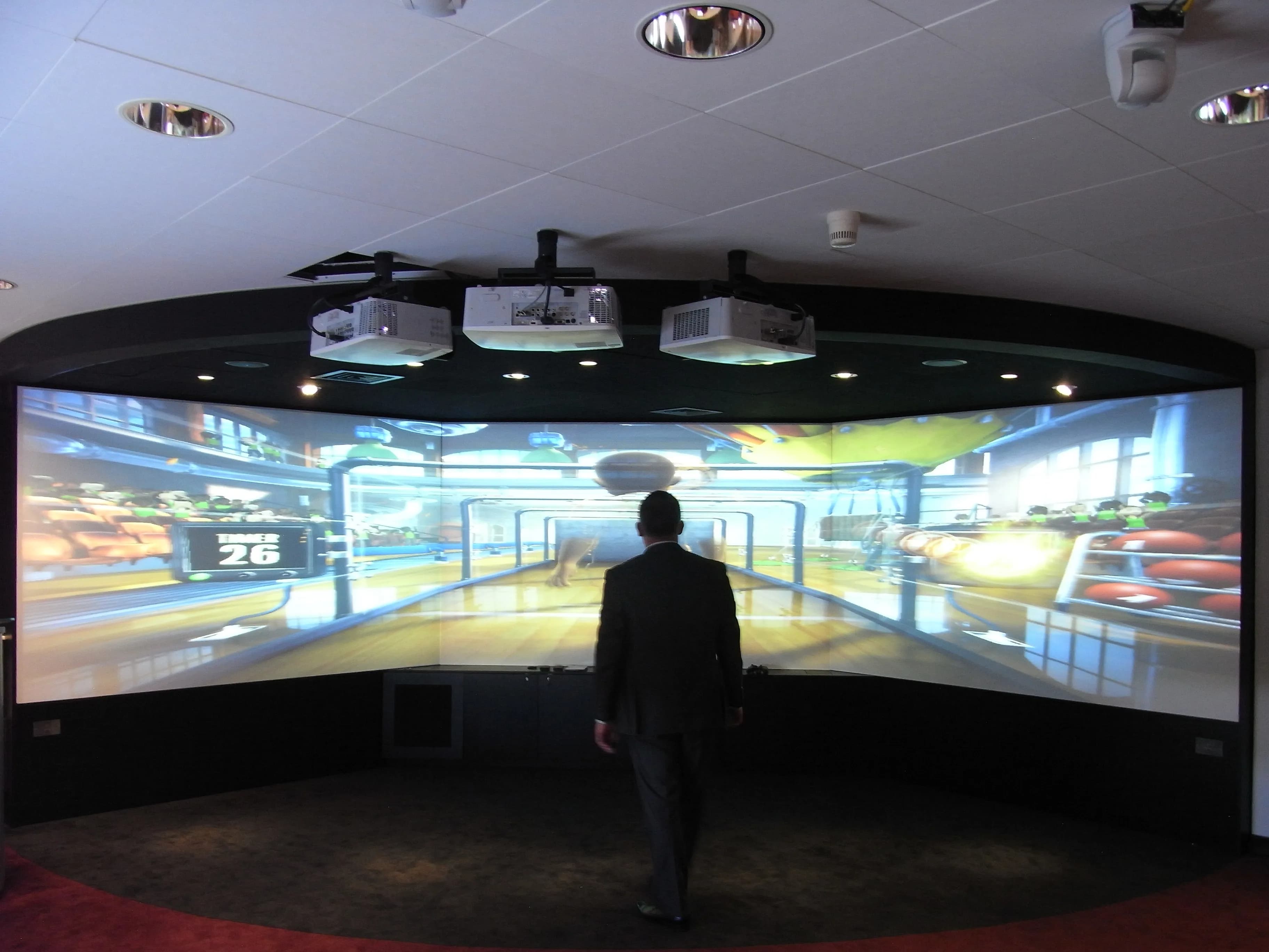 Man in a suit stands before a large curved screen displaying a virtual sports simulation.